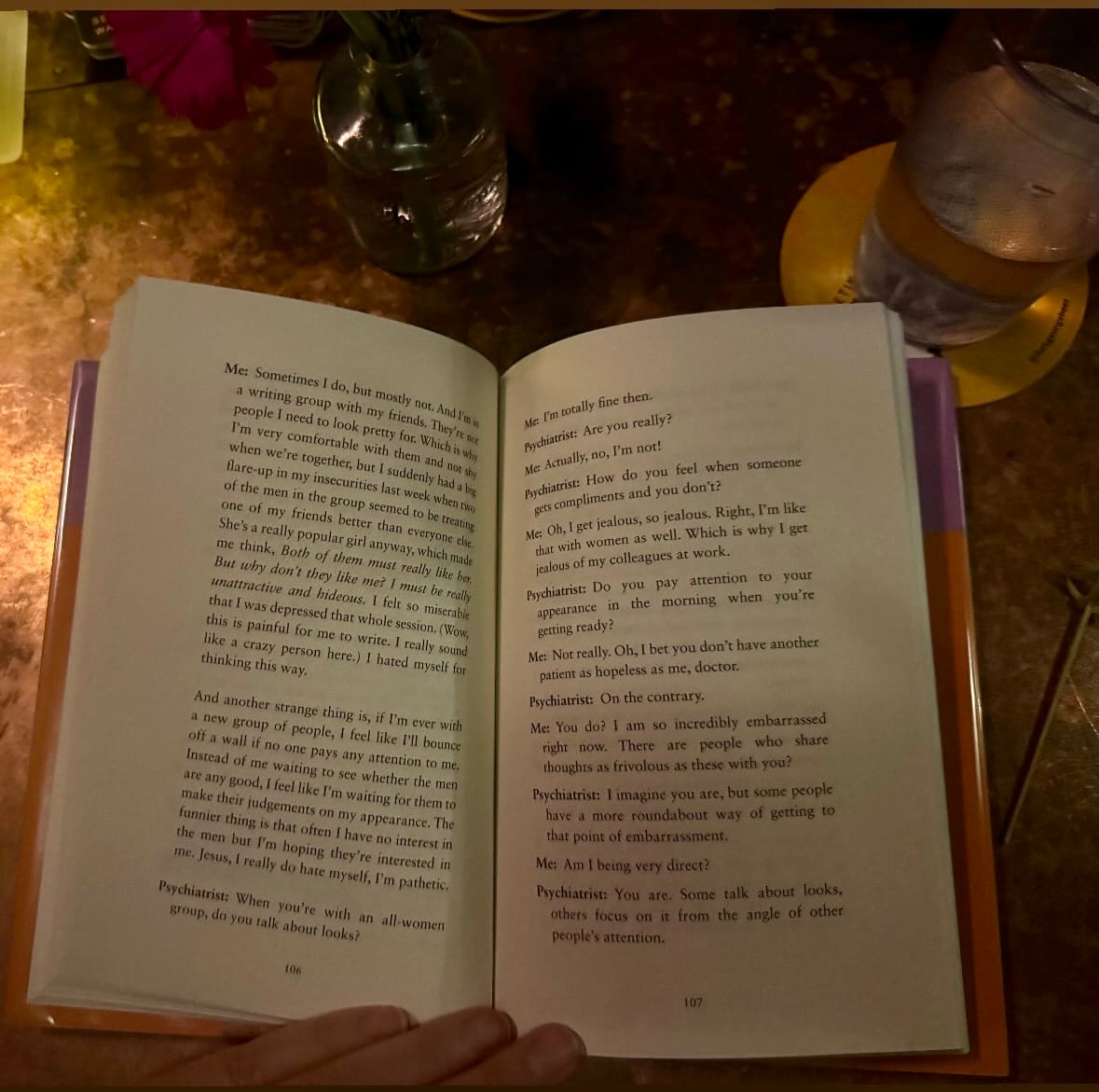 An open book near a glass of water at a bar top 
