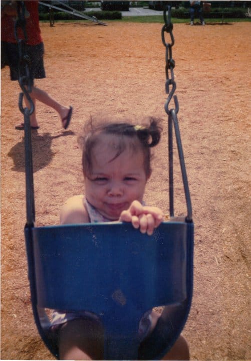 Little girl making a funny face in a swing at a park